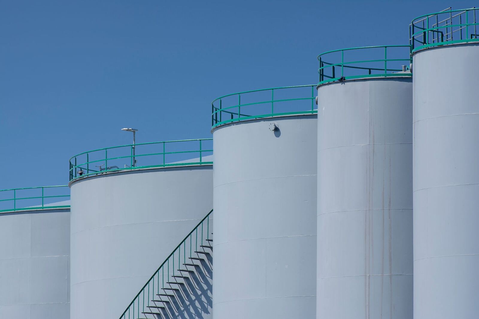 Large industrial storage tanks with green railings against a clear blue sky.